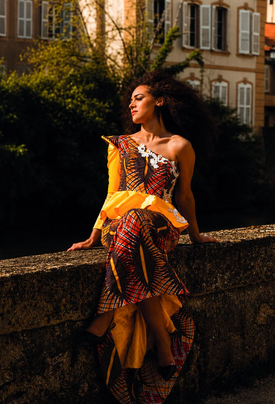 Robe en wax orange Maison 3 Points, assise sur un muret de pierre